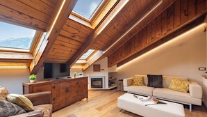 Um quarto com pé direito alto, vigas de madeira, lareira, sofá e televisão.