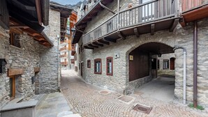 Uma rua de paralelepípedos estreita, ladeada por edifícios de pedra com varandas de madeira e portas em arco.