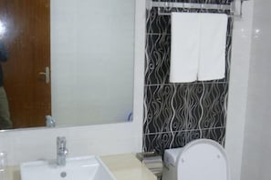 A bathroom with a sink, mirror, toilet, and patterned shower wall.