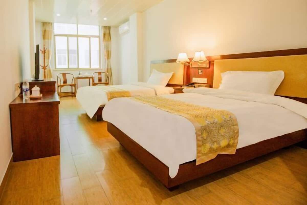 A hotel room with two beds, a wooden desk, a chair, a nightstand with lamps, and a window with curtains.