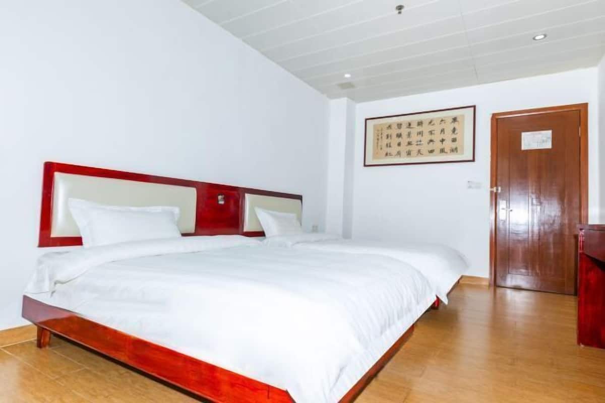A hotel room with a large bed, wooden headboard, white bedding, a wooden door, and a framed picture on the wall.