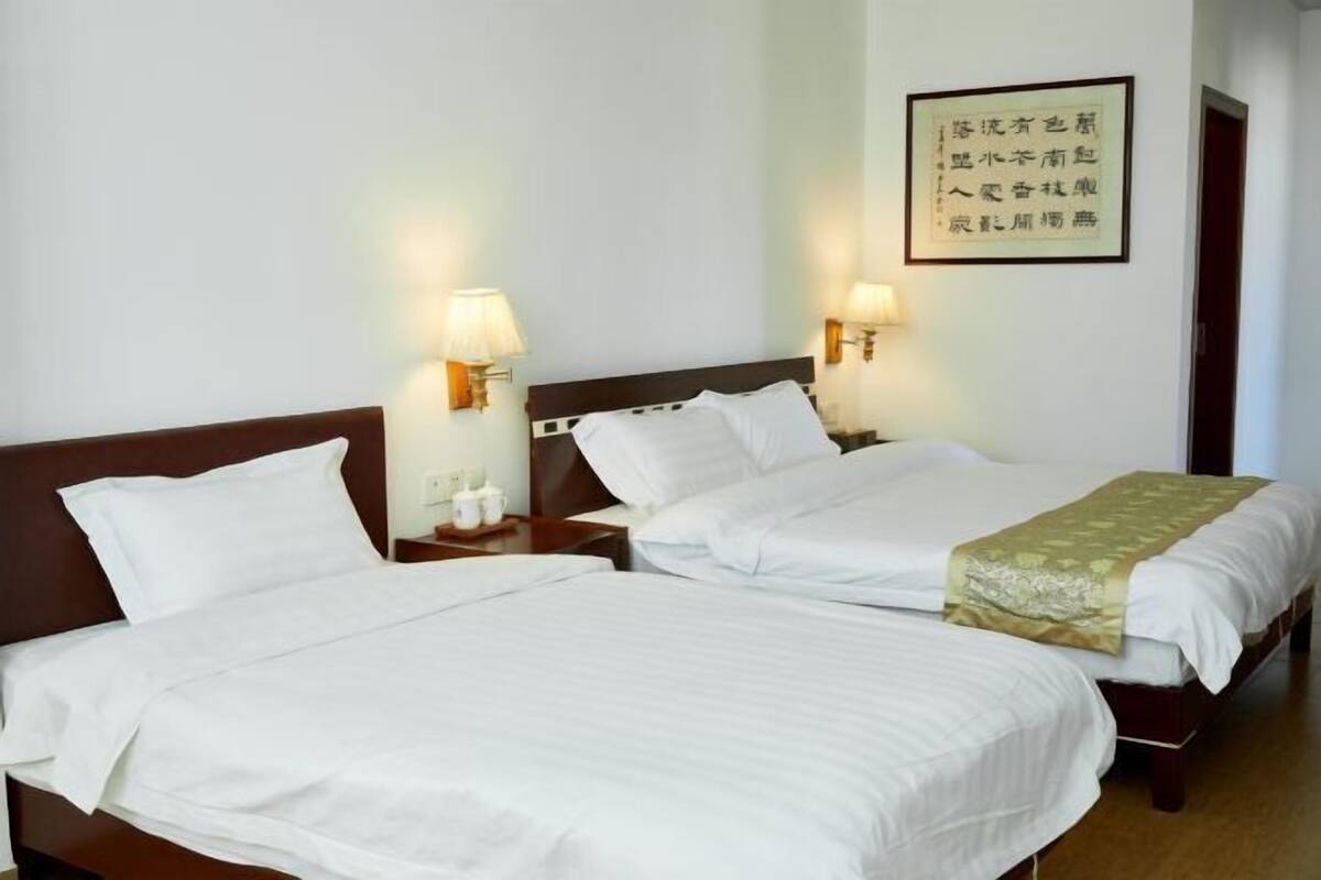 A hotel room with two single beds, bedside tables with lamps, and a framed quote on the wall.