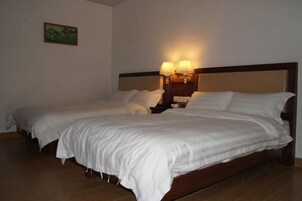 Cama doble con ropa de cama blanca, dos lámparas de noche y una mesita de noche.