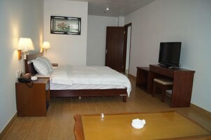 Habitación de hotel con cama, lámparas de noche, escritorio con televisor y una mesita con vela.