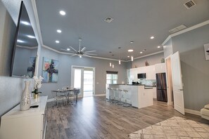 Una cocina moderna con una isla central, taburetes de bar y un comedor con mesa de vidrio.