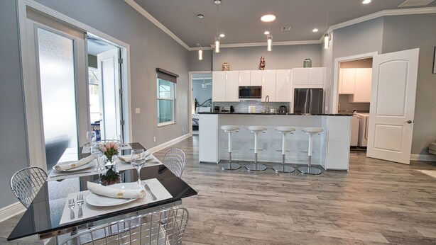 A modern kitchen with white cabinets, a central island with bar stools, and a dining area with a glass table and metal chairs. - 7 min to the Beach. Family Venice Beach Retreat. Private Saltwater Screened Pool (Venice)