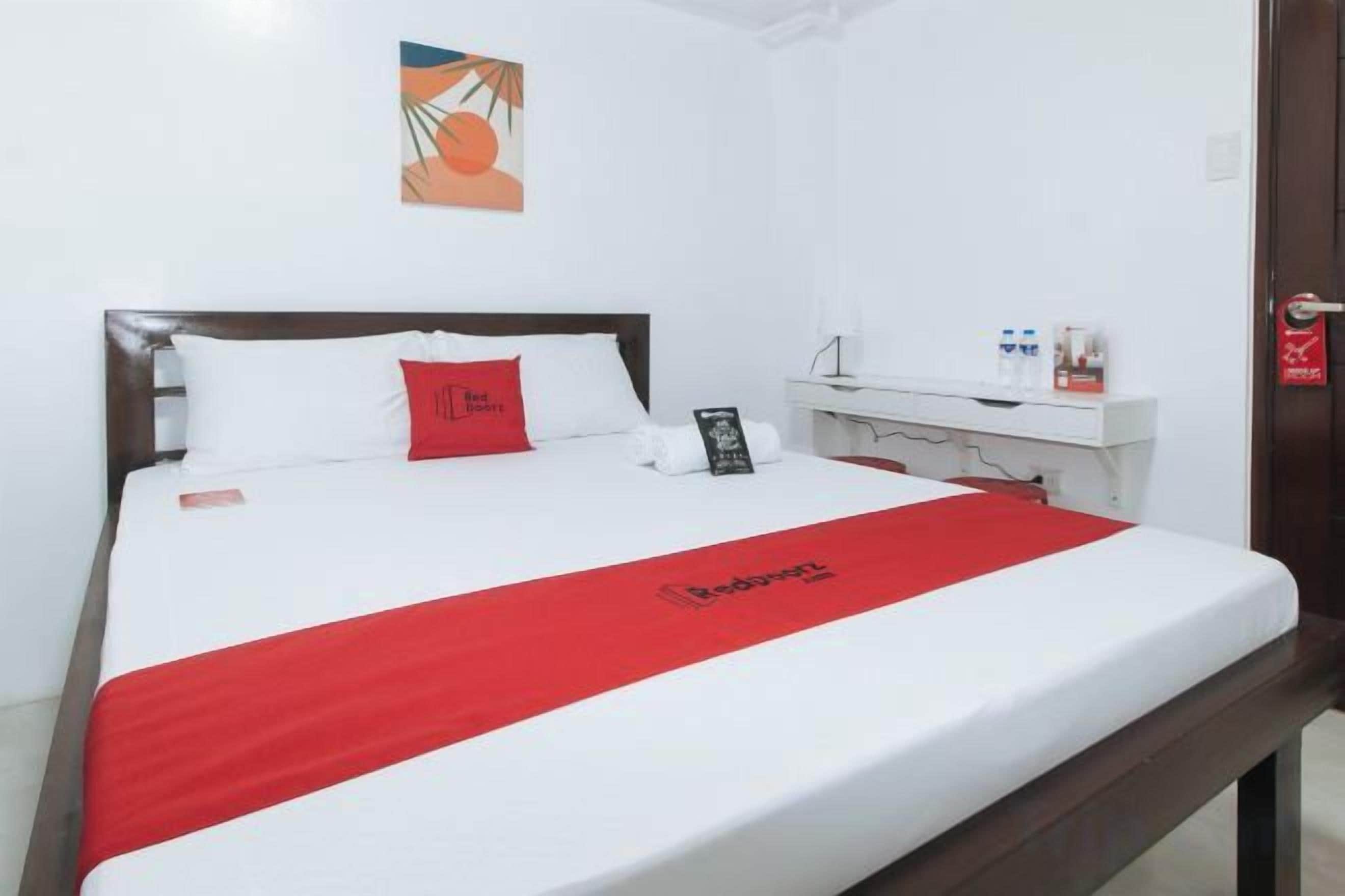 Quarto de hotel com uma cama, mesa de cabeceira com telefone, travesseiro vermelho e manta vermelha.