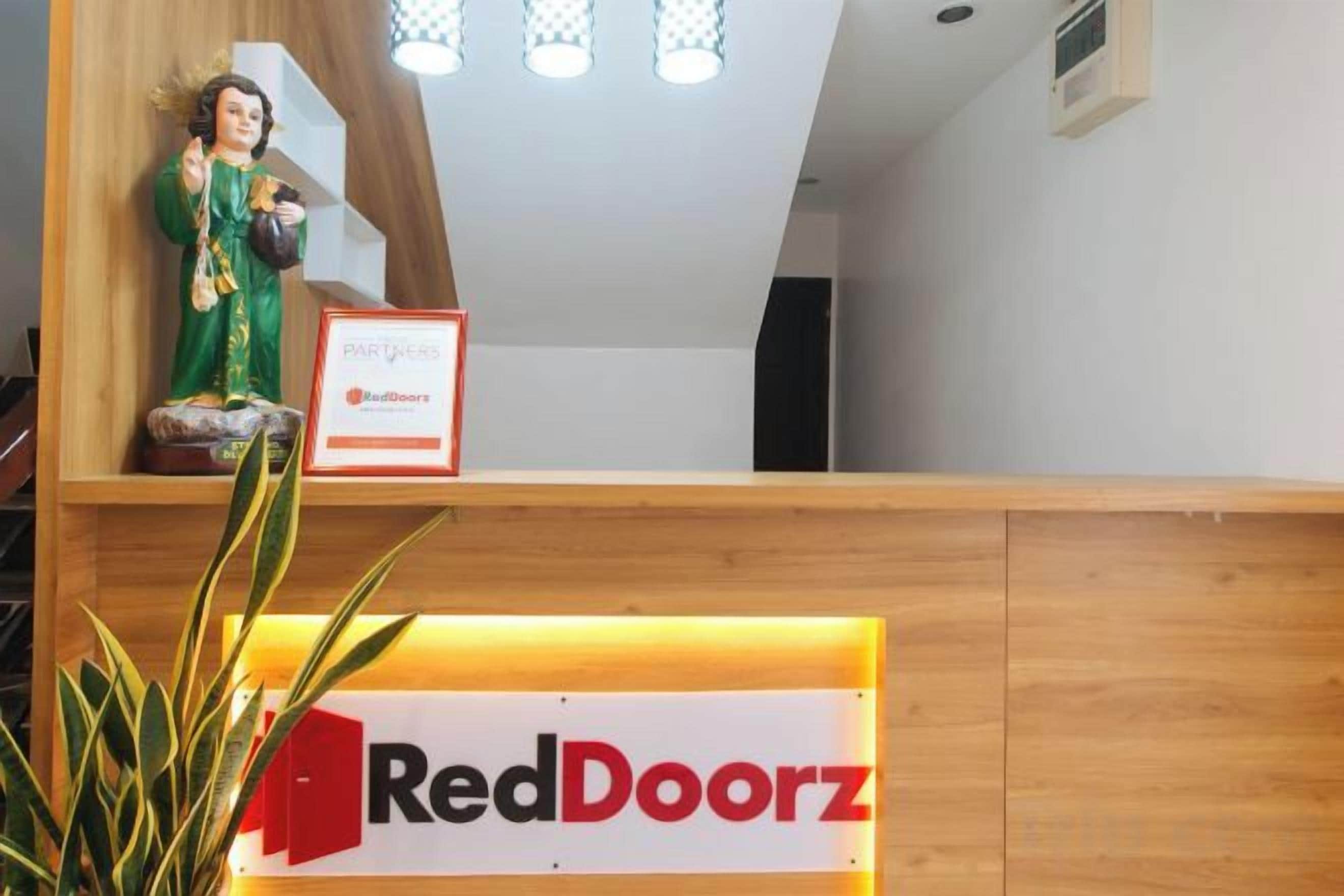 Uma receção com o letreiro RedDoorz, uma estátua e uma planta.