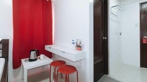 A small room with a white desk, two red stools, a red curtain, a white shelf with items, and a dark door. - RedDoorz near UST Sampaloc Manila (City of Manila)