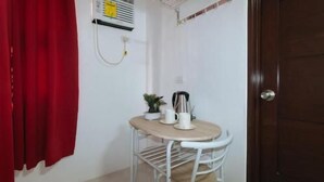 A small room with a table, chair, red curtains, a wall-mounted heater, and a door. - RedDoorz near UST Sampaloc Manila (City of Manila)