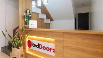 Balcão de recepção com a placa RedDoorz, uma estátua e uma escadaria.