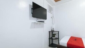 A hotel room with a bed, a TV mounted on the wall, a small table with a plant, and a red blanket on the bed. - RedDoorz near UST Sampaloc Manila (City of Manila)