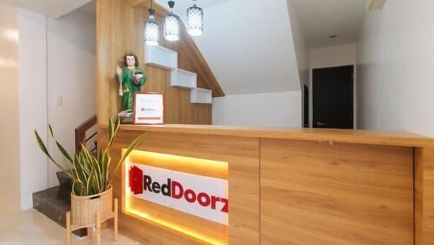 A reception desk with a RedDoorz sign, wooden paneling, a potted plant, and a staircase. - RedDoorz near UST Sampaloc Manila (City of Manila)