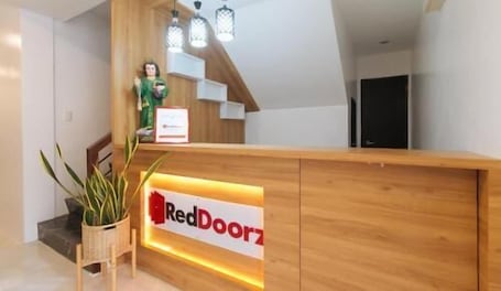 A reception desk with a sign reading 'RedDoorz,' a wooden reception desk, a plant, and a staircase.. RedDoorz near UST Sampaloc Manila