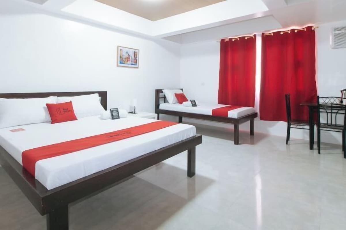 Una habitación de hotel con una cama grande, una cama más pequeña, un escritorio y cortinas rojas.