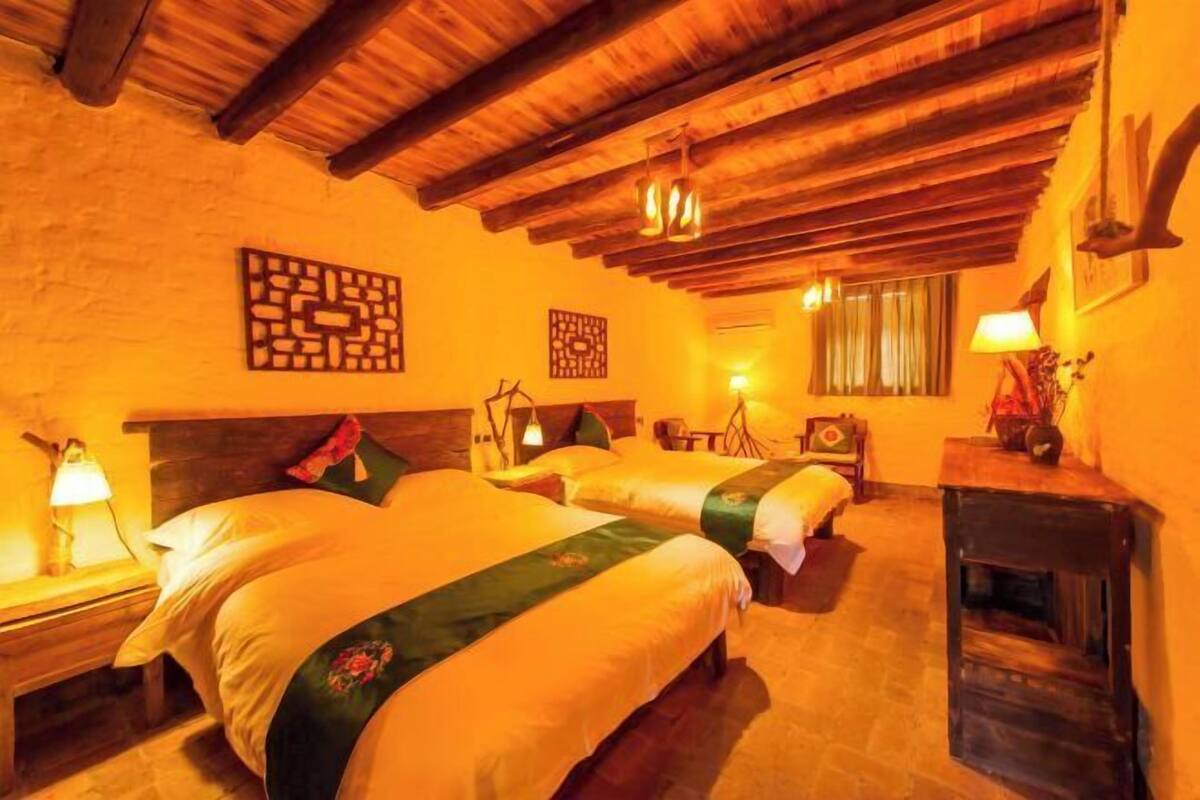 A cozy room with three beds, wooden beams on the ceiling, and a fireplace.