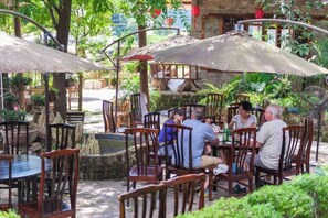 An outdoor café with wooden tables and chairs, surrounded by greenery and stone walls. - Yangshuo Countryside Washe Inn (Yulonghe Scenic Area) (Yangshuo)