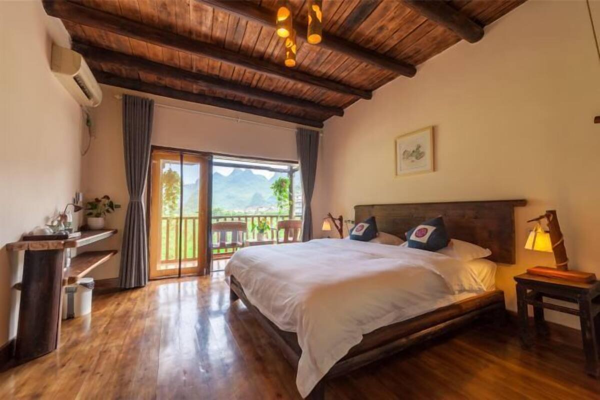 A bedroom with a wooden ceiling, a bed with white bedding, a nightstand, and a window with a view.