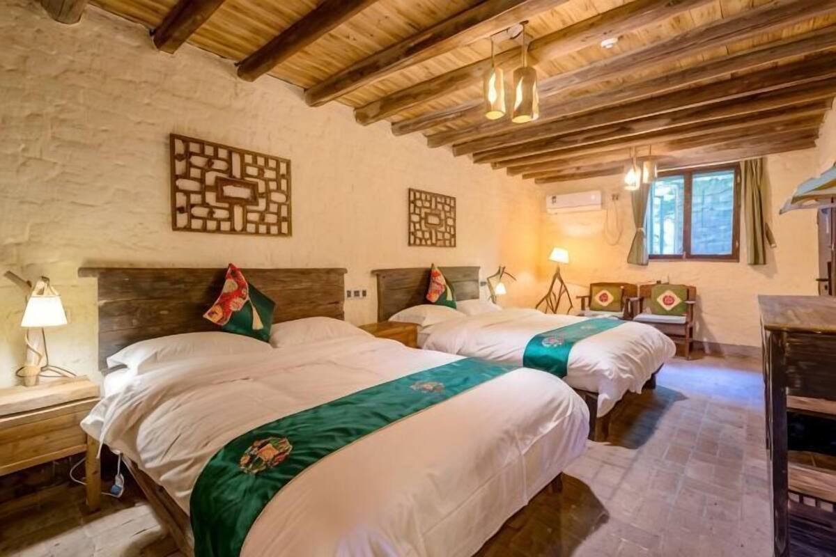 A room with two beds, wooden beams on the ceiling, and a stone wall.
