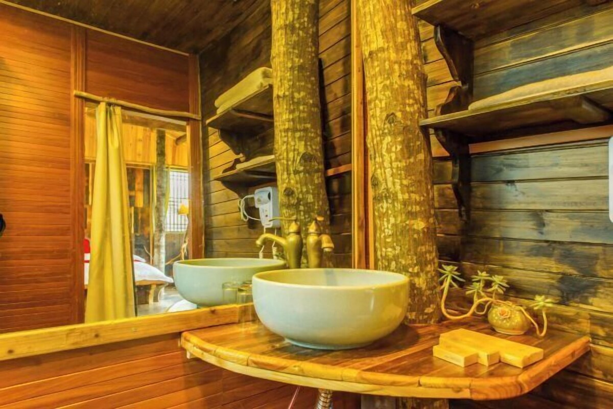 Ein Holzblockhaus-Interieur mit einem hölzernen Waschtisch, zwei großen Schüsseln, einem Spiegel und einem kleinen Regal mit Pflegeprodukten.