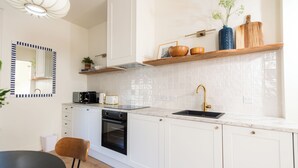 Une cuisine moderne avec des meubles blancs, un four noir, un évier doté d’un robinet doré et un plan de travail en bois.