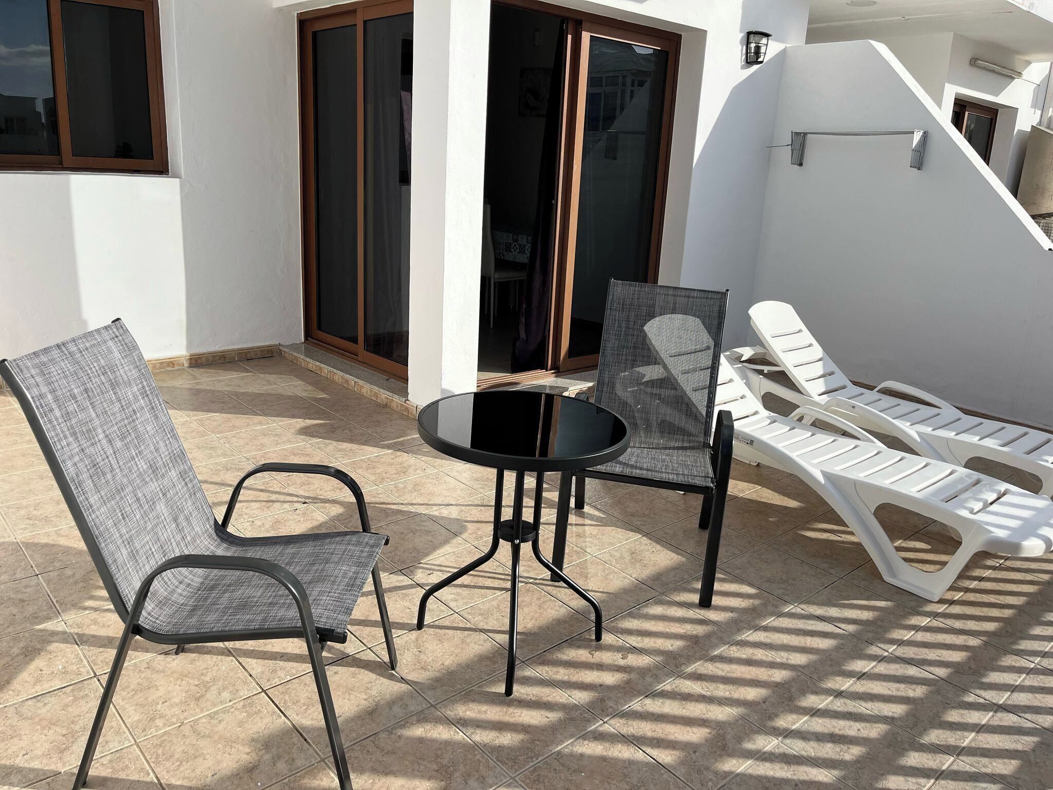 Un patio con una mesa, dos sillas y una butaca blanca, además de un ventanal corredero.