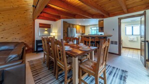 A spacious dining area with a wooden table and chairs, a kitchen in the background, and a high ceiling with exposed beams.