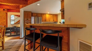 A kitchen with wooden cabinets, a stainless steel refrigerator, and a bar area with two black barstools.