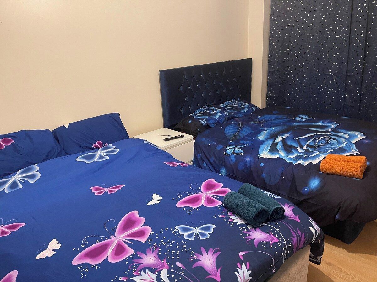 Two beds with floral and butterfly bedding, a nightstand, and a dark headboard.