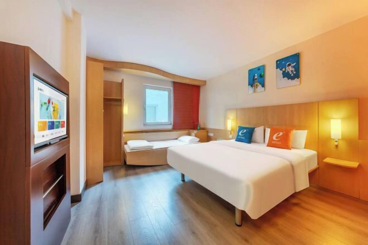 A hotel room with a large bed, a TV, a desk, and a window.
