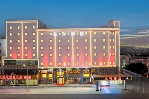 Et hotel med flere etager, en markant indgang med et overdækket område og oplyst skiltning.
