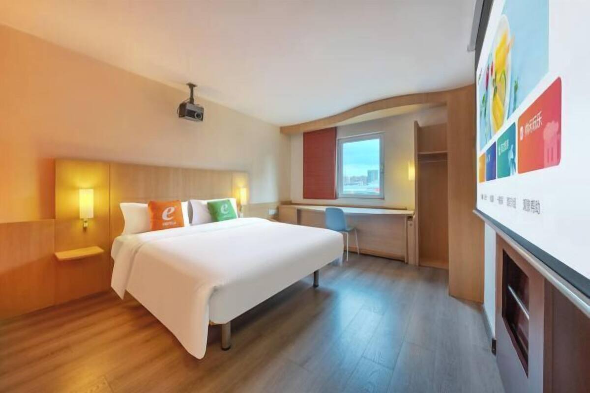 A hotel room with a bed, a desk, a chair, a TV, and a window.