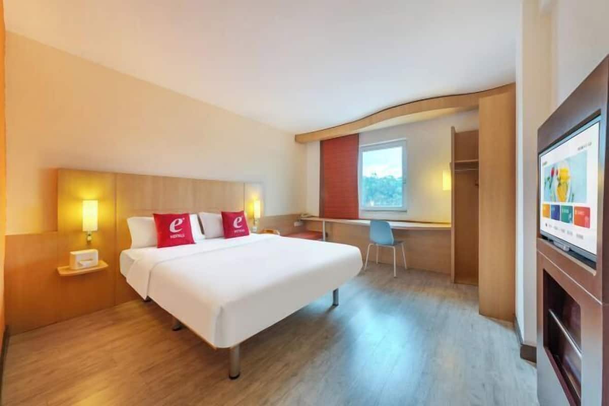 A hotel room with a bed, bedside table, lamp, desk, chair, and a TV screen.