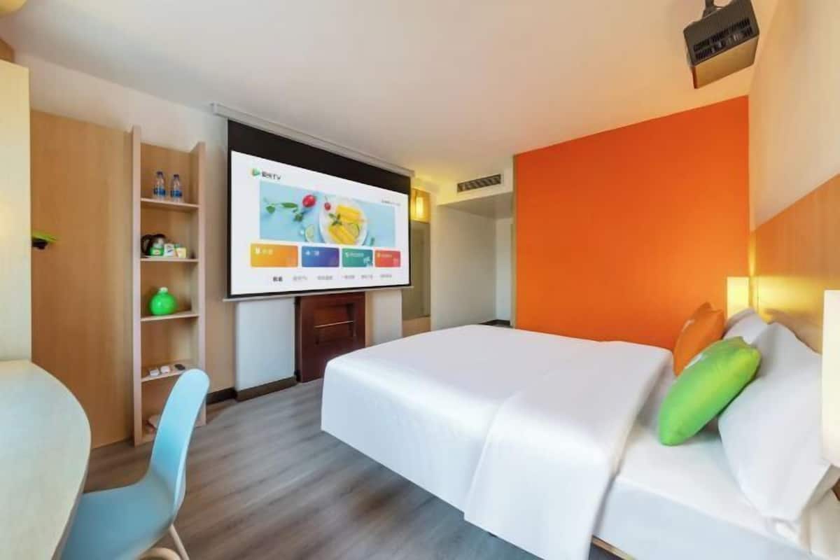 A hotel room with a bed, a TV screen, a desk, and a chair.