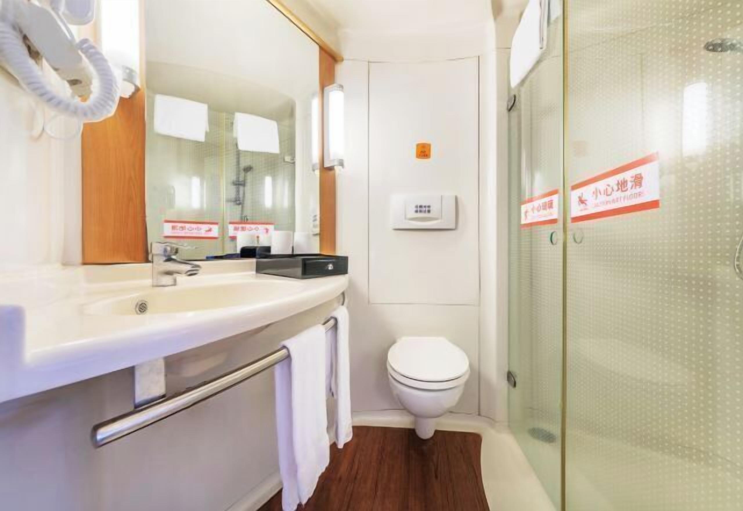 A modern bathroom with a white sink, mirror, and toilet. There is a towel rack with a towel hanging, and a glass shower enclosure.