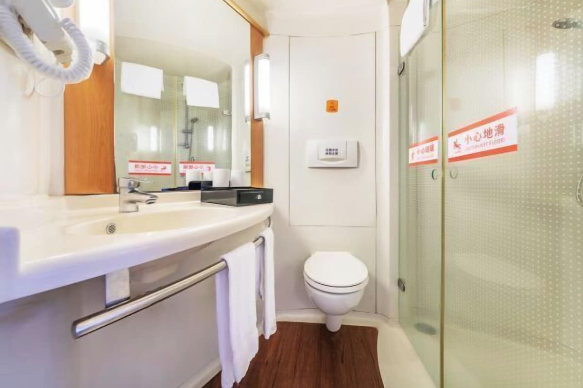 Une salle de bain moderne avec un lavabo blanc, un miroir et des toilettes. On y trouve un porte-serviettes avec une serviette suspendue, ainsi qu’une cabine de douche en verre.