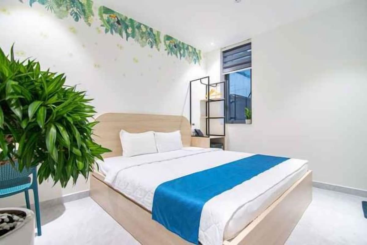 A bedroom with a bed, a nightstand, a potted plant, and a window.