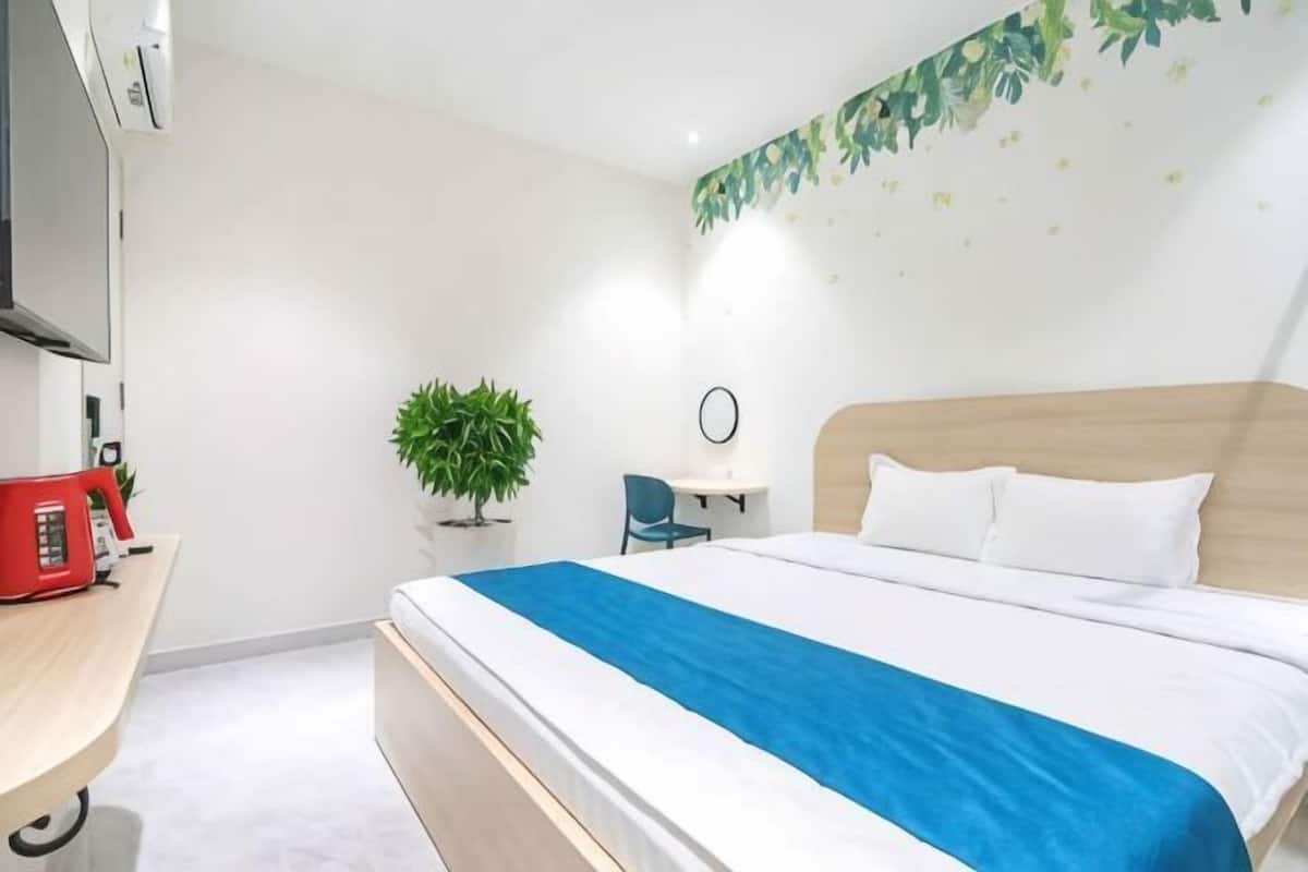 Ein Hotelzimmer mit einem Bett, einem Schreibtisch mit rotem Telefon, einem kleinen Tisch mit Pflanze und einem an der Wand montierten Fernseher.