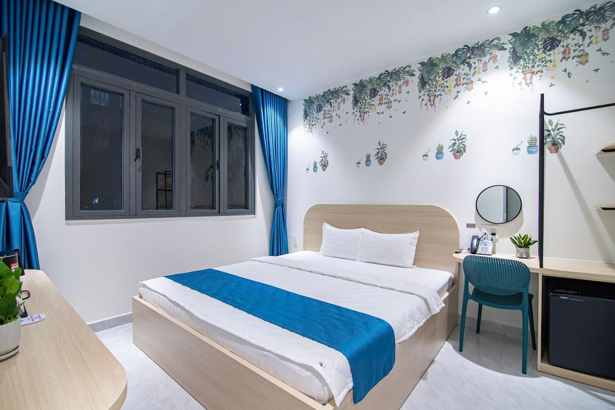 Ein modernes Schlafzimmer mit Bett, Schreibtisch, Stuhl, kleinem Kühlschrank und einem Fenster mit Vorhängen.