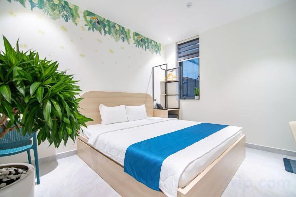 A bedroom with a bed, a potted plant, a nightstand, and a window.