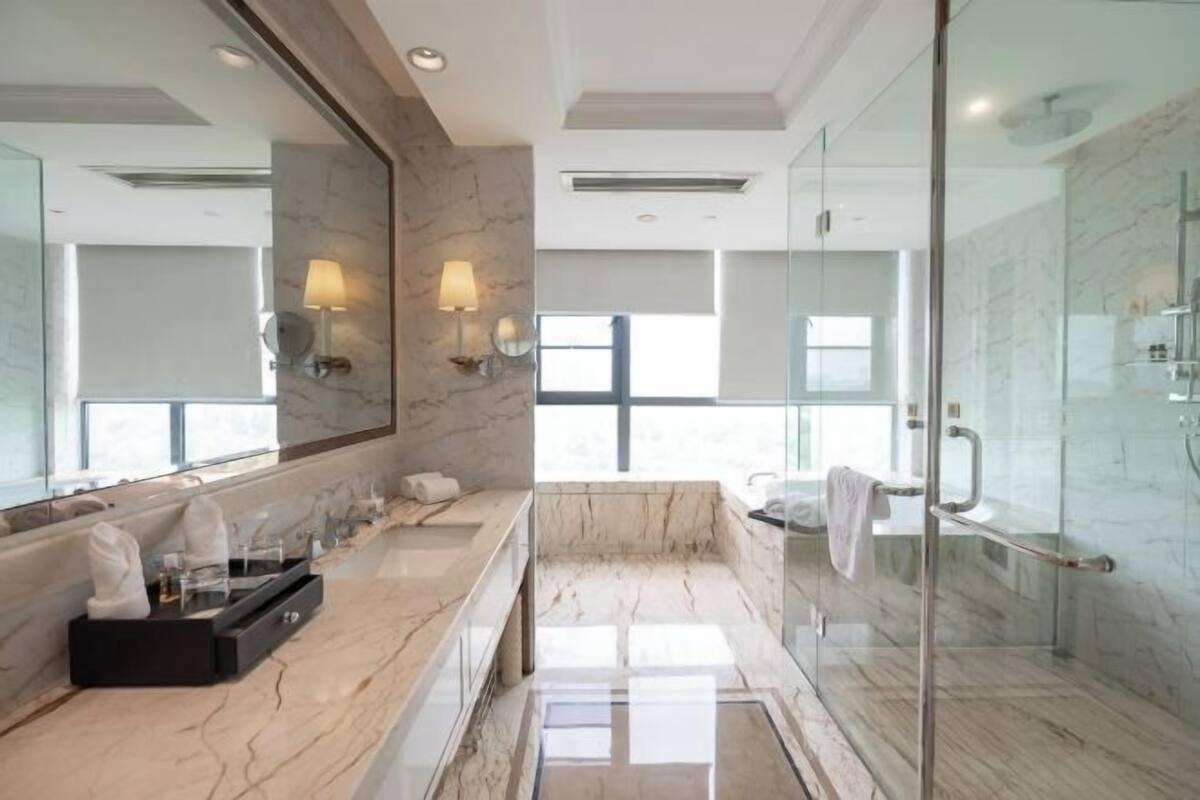 Een moderne badkamer met een grote spiegel, marmeren aanrechtbladen, een douchecabine van glas en uitzicht op het groen.