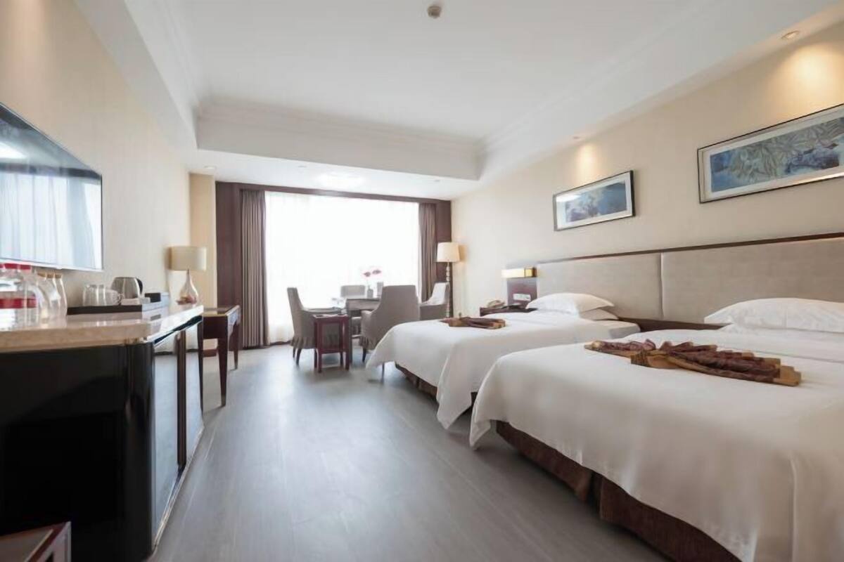Een hotelkamer met twee bedden, een bureau, een stoel en een eettafel.