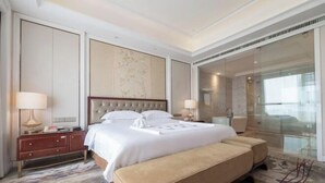 A hotel room with a large bed, a bedside table, a bench, a glass shower enclosure, and a view of the outside. - Fairyland International Hotel (Xiantao)