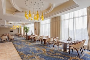 Um hall de hotel espaçoso, com um amplo tapete, diversas mesas de jantar e uma grande janela com cortinas.