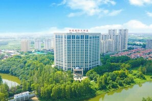 A high-rise hotel with a central courtyard, surrounded by greenery and a body of water.
