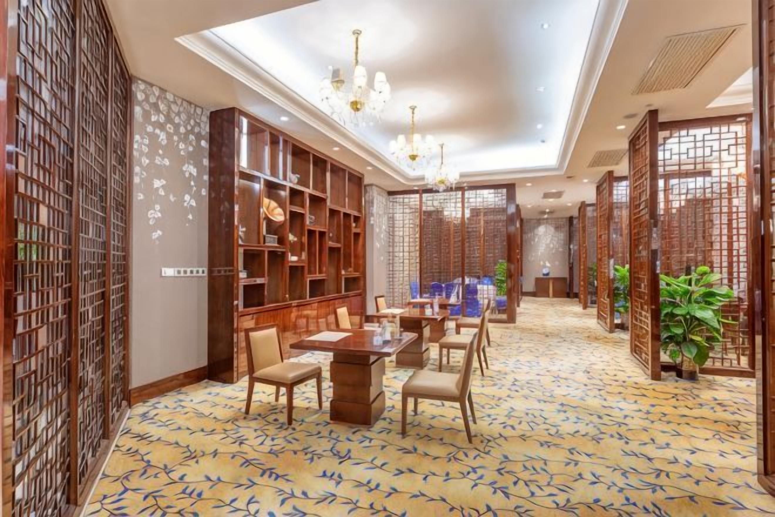 A hotel room with a dining area, a large bookshelf, and a patterned carpet.