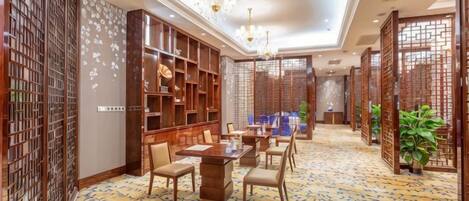 A hotel room with a dining area, a large bookshelf, and a patterned carpet.