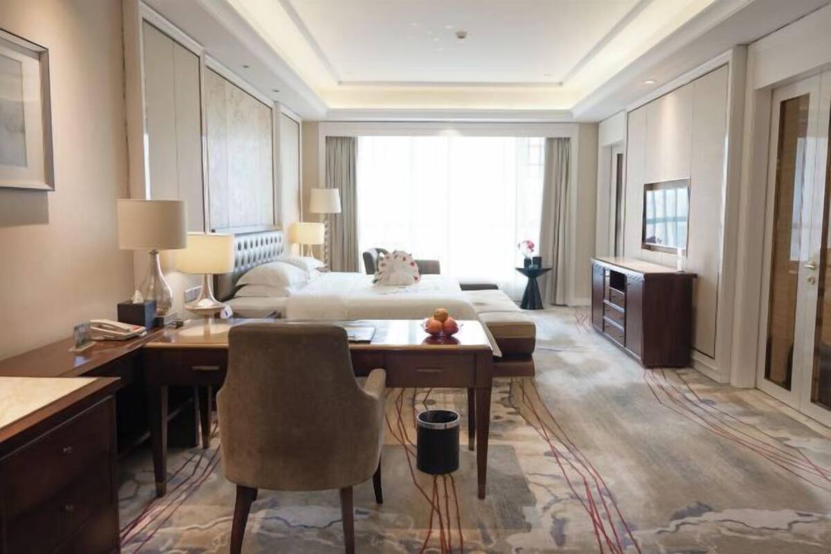 Een hotelkamer met een bed, bureau, stoel, lamp, televisie en een vloerbedekking.