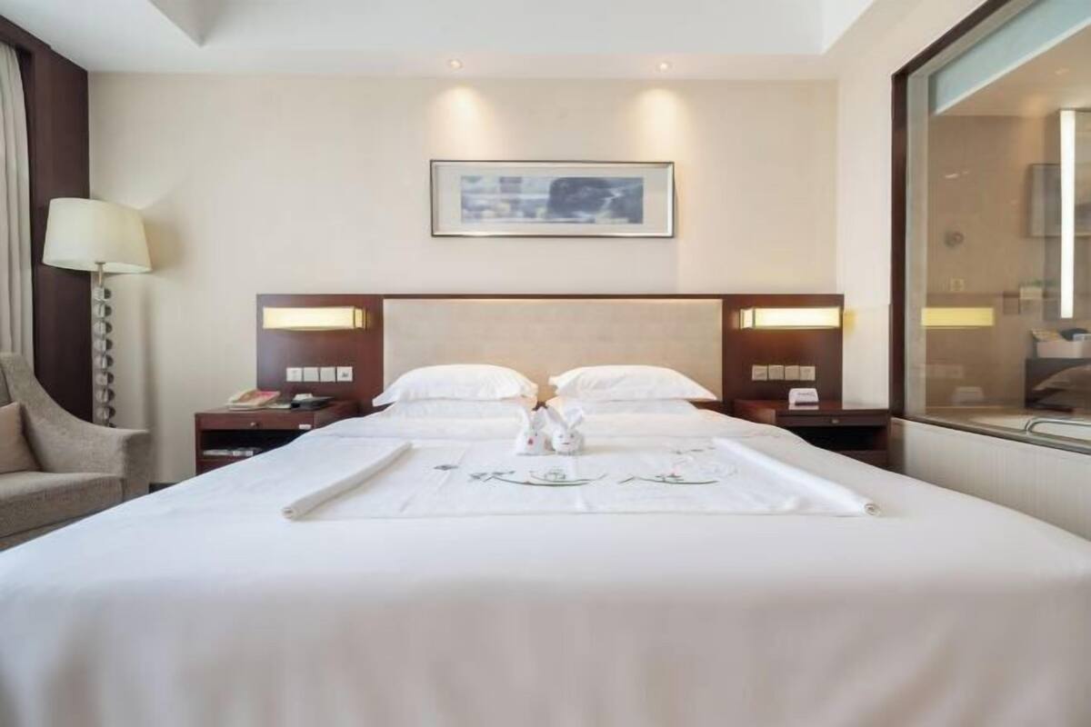 Een hotelkamer met een groot bed, twee nachtkastjes, een lamp, een lijst met een foto aan de muur en een raam.
