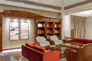 A hotel lobby with a curved wooden wall, a seating area with a red sofa and white chairs, a coffee table, and a bookshelf. - Fairyland International Hotel (Xiantao)